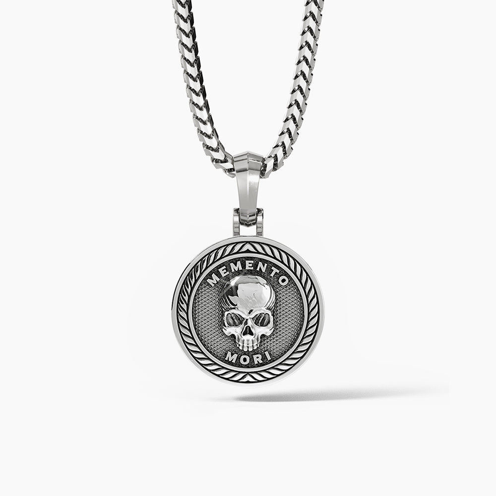 a silver skull pendant in the shape of a medallion with the words memento mori inscribed