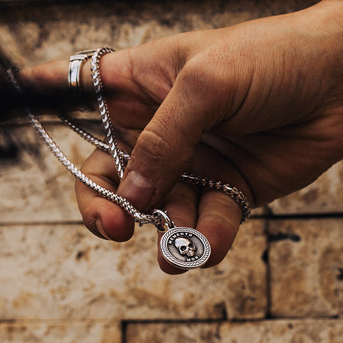 silver memento mori skull pendant on a silver chain held in a hand