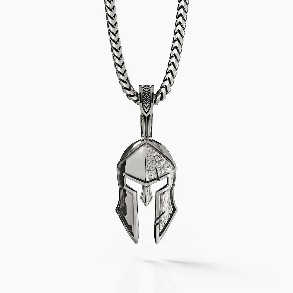 a silver Spartan pendant in the shape of a helmet with one side battle worn