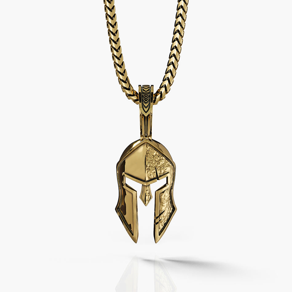 a gold Spartan pendant in the shape of a helmet with one side battle worn