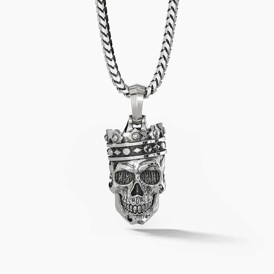 a cool silver mens pendant in the shape of a skull wearing a crown hangs from a necklace