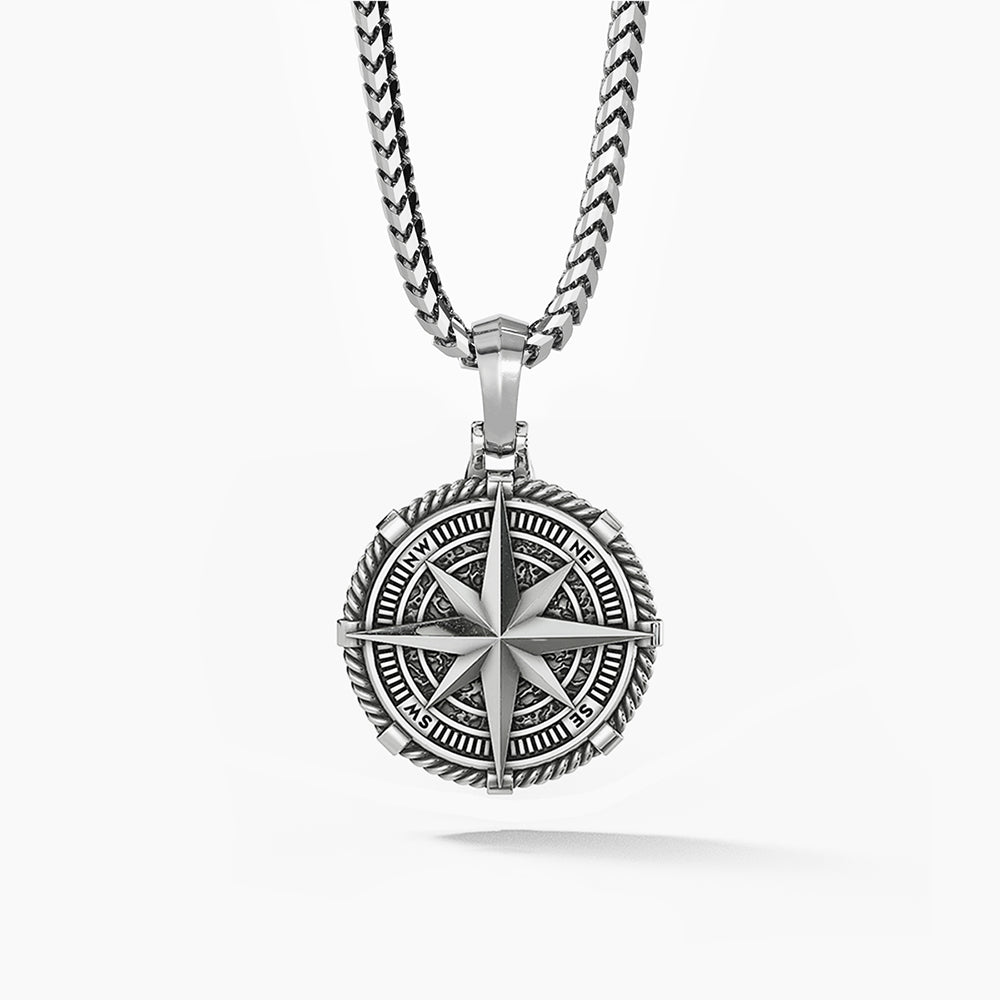 a detailed silver compass pendant hangs from a silver chain