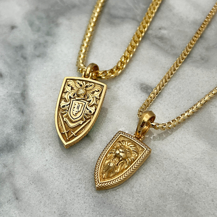 two gold lion pendants lying on white marble. One of them shows a knight's helmet, crest patterns and swords on the back