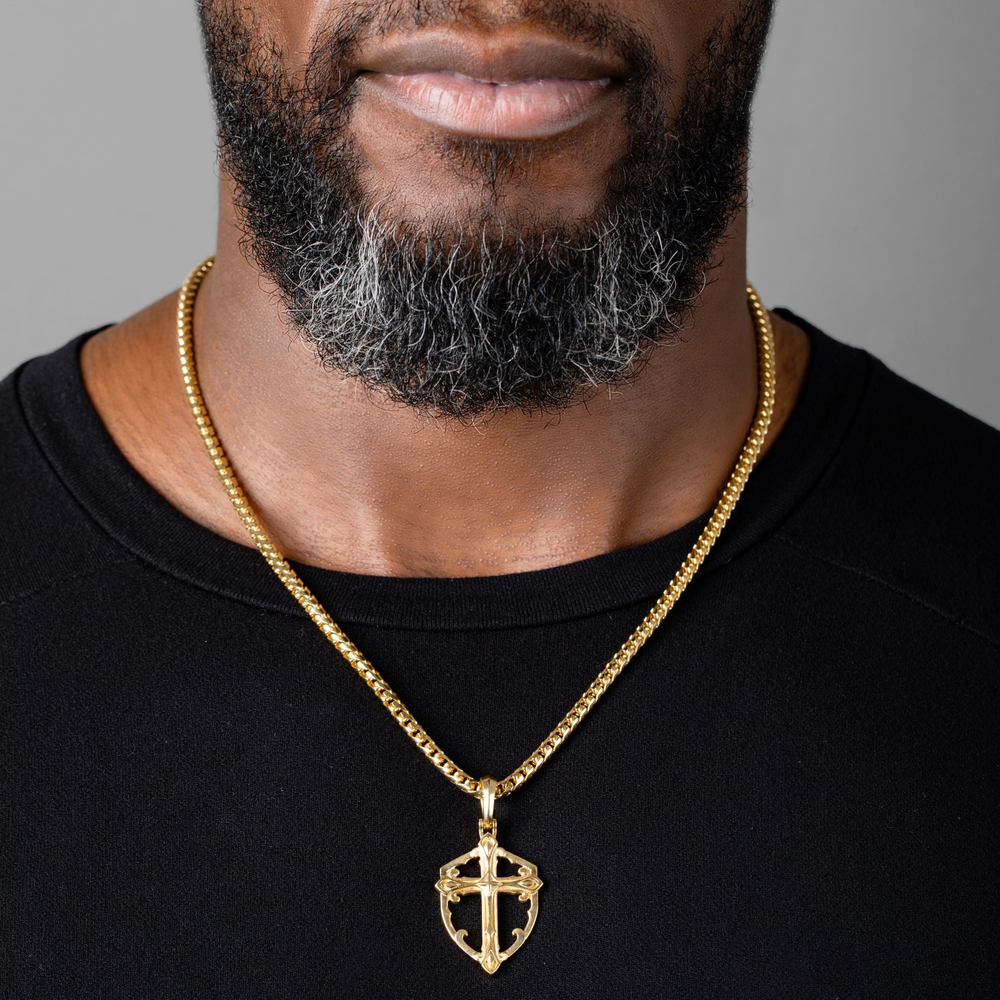 man wears a gold cross necklace shaped like a shield and a gold franco chain