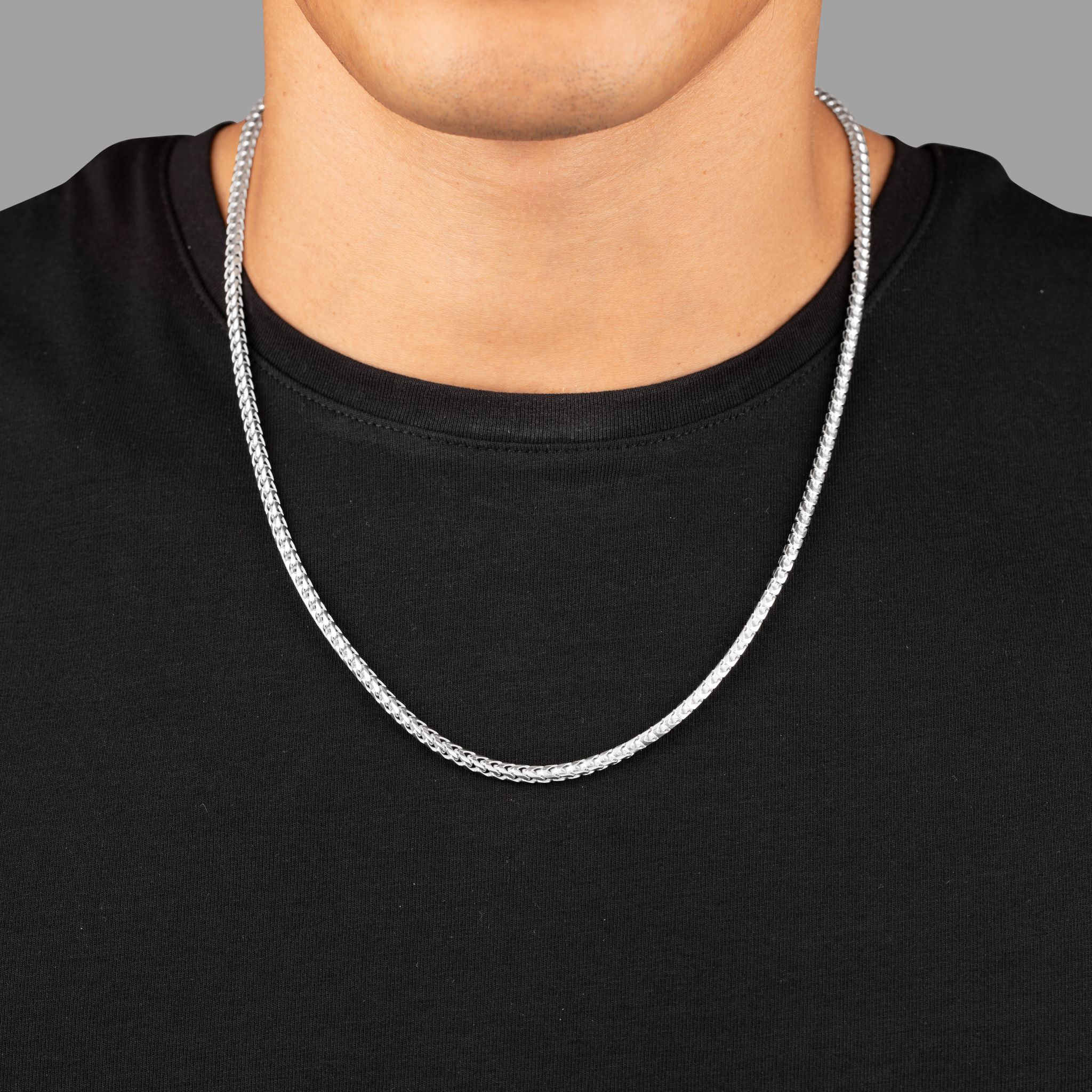 a close view of a man in a black shirt wearing a 3mm silver franco chain