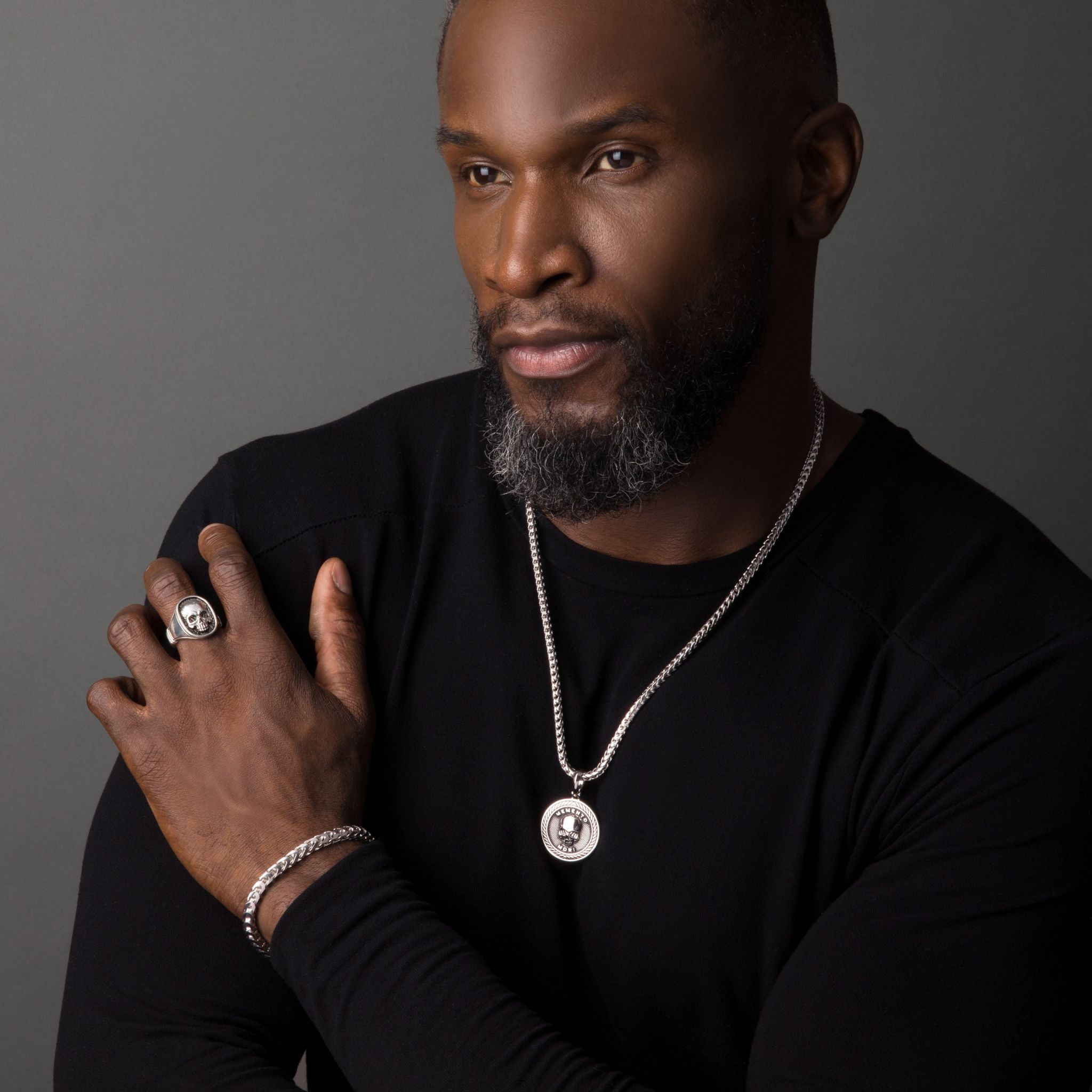 a man wears a shiny round silver skull pendant and matching skull signet ring