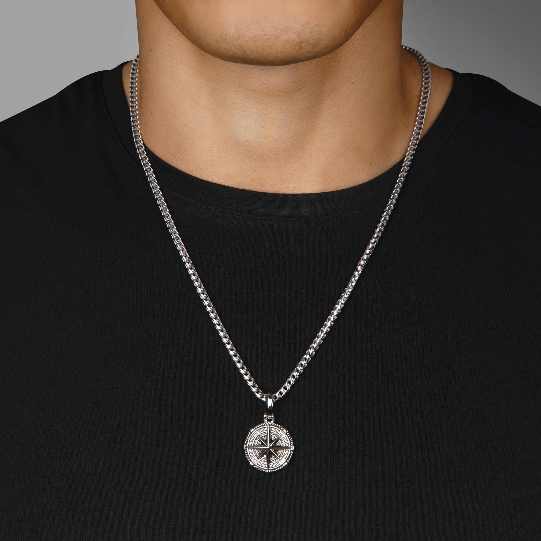 a man in a black shirt wears a silver compass necklace