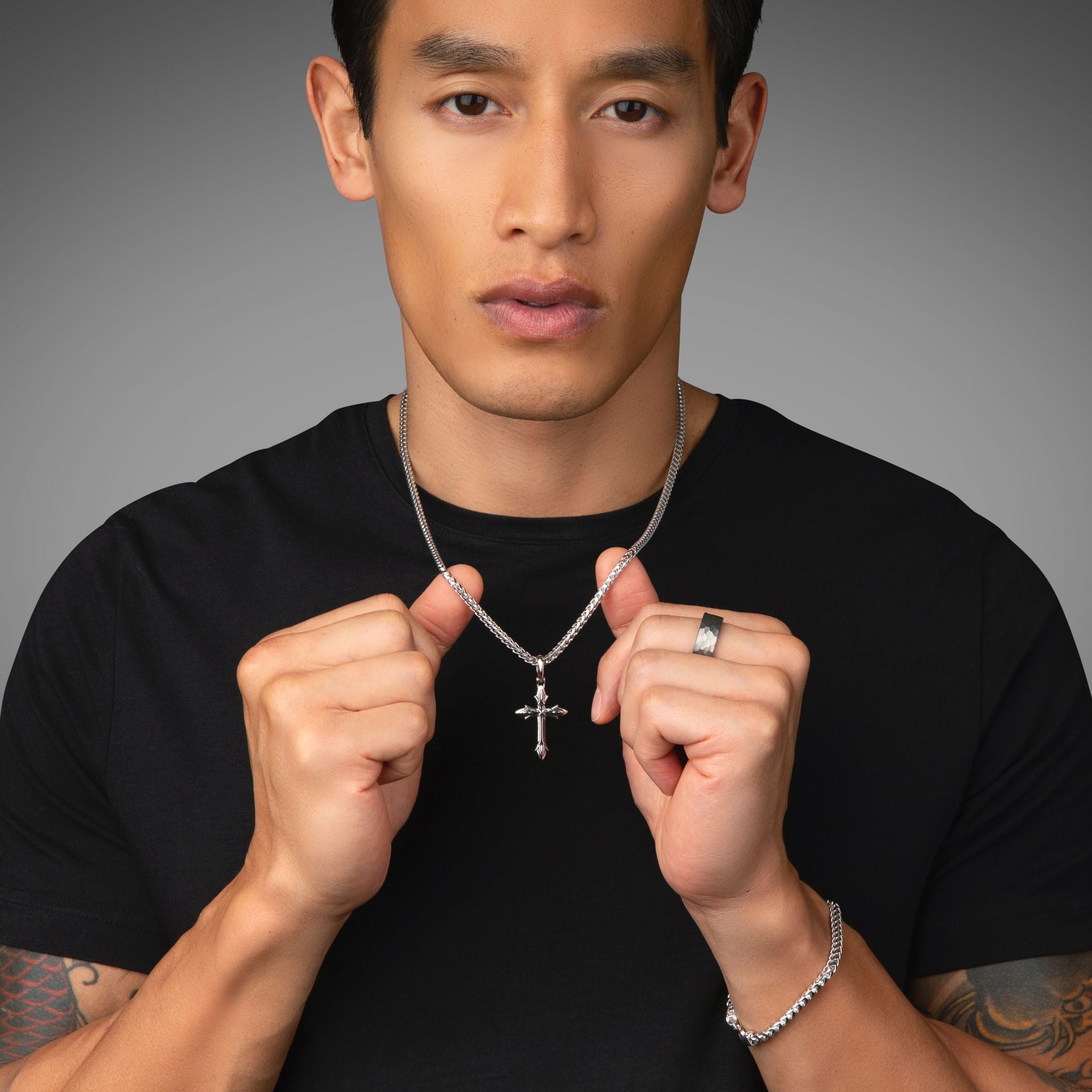 a handsome man shows the silvercross necklace he's wearing
