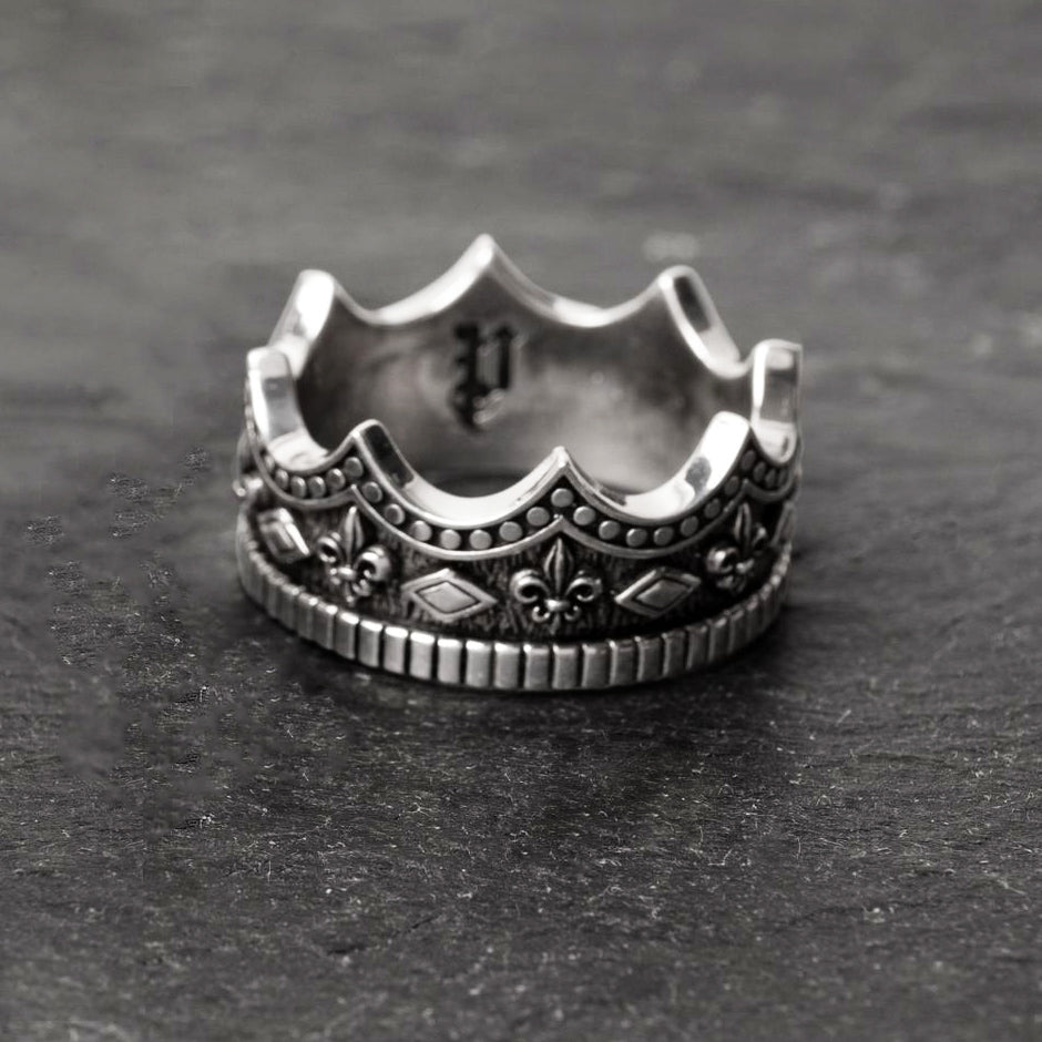 crown-shaped mens silver wedding band lays on a slate surface